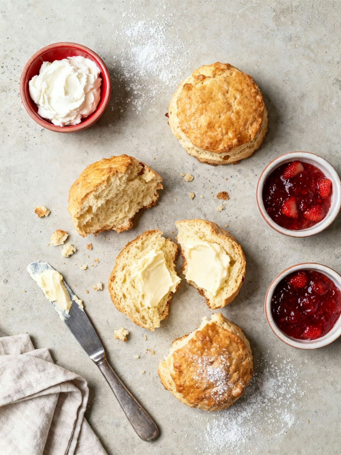 Buttermilk scones split open with butter, cream and strawberry jam